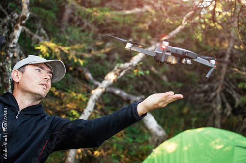 Young man with flying drone at camping tent in the background
