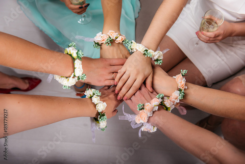 The girlfriends of the bride and the bride are sitting in a circle and holding hands. Hands are decorated with flower bracelets.