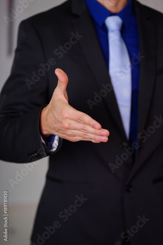 Close up of man wearing a suit with his open hand in front of him, in a blurred background