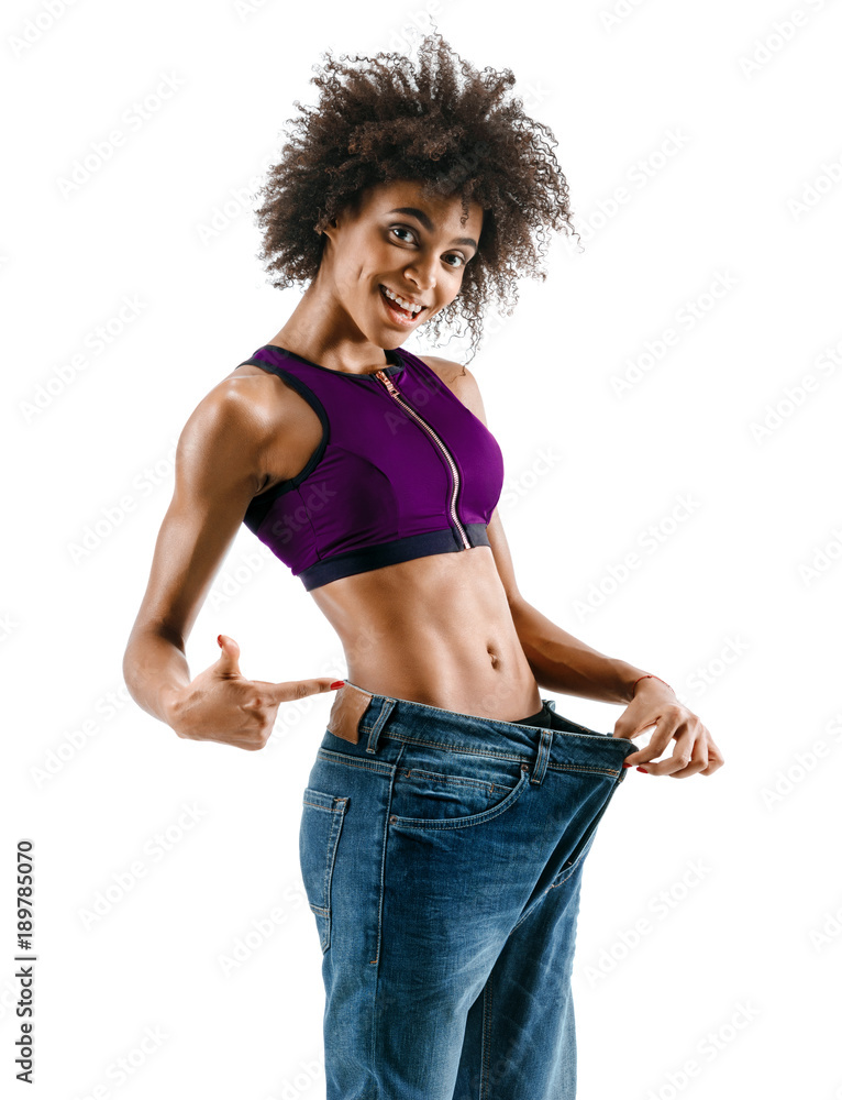 Sporty girl pulling her big jeans and showing weight loss. Photo of african  girl on white background. Strength and motivation Stock Photo | Adobe Stock