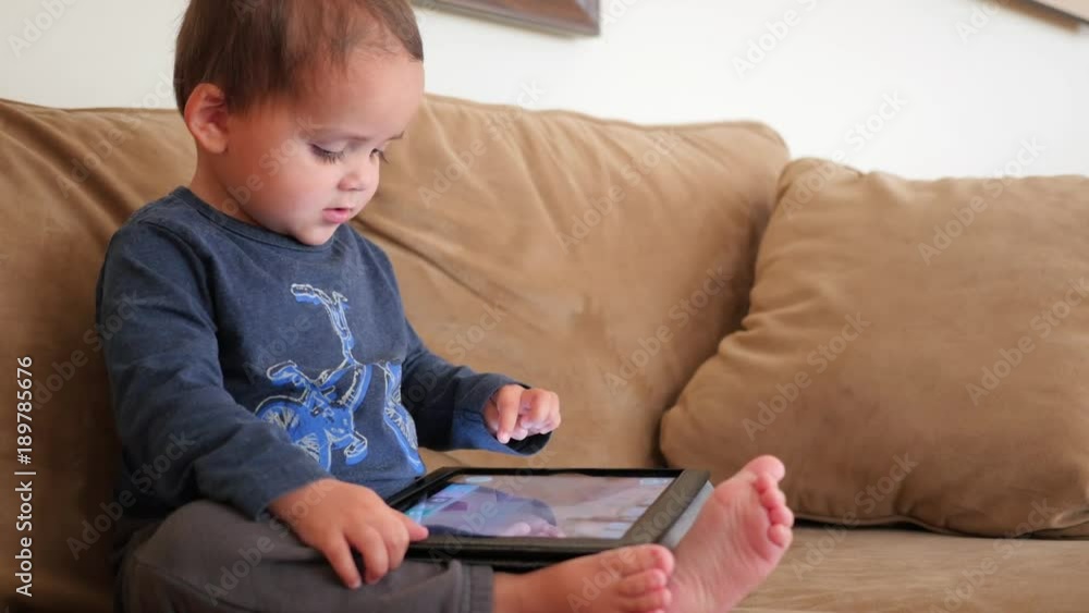 An adorable boy toddler playing with an ipad on the couch An adorable boy toddler playing with an ipad on the couch