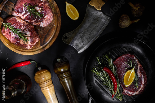 Fresh raw meat. Beef Tenderloin and marbled beef steaks on grill pan and frying board with seasoning, black background top view.