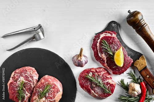 Fresh raw beef steaks with herbs, garlic, olive oil, pepper, salt and rosemary on black board: Tenderloin, Striploin, Rib Eye photo