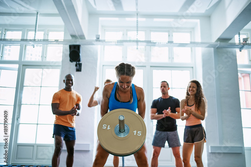 Woman weightlifting with friends encouraging her in the backgrou