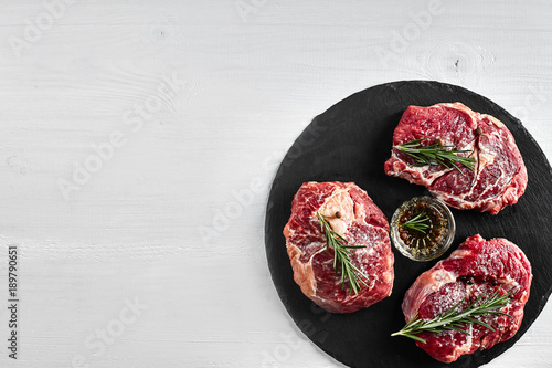 Fresh raw beef steaks with herbs, garlic, olive oil, pepper, salt and rosemary on black board: Tenderloin, Striploin, Rib Eye photo