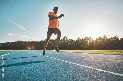 Focused young athlete sprinting alone along a running track