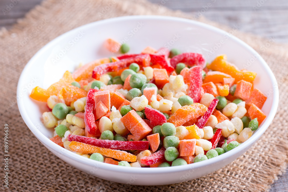 Mixed frozen vegetables in a plate on wooden table Mixed frozen vegetables in a plate on wooden table