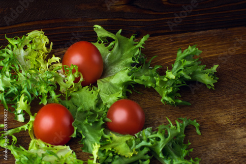 fresh red tomatoes with green lettuce leaves on an old wooden countertop