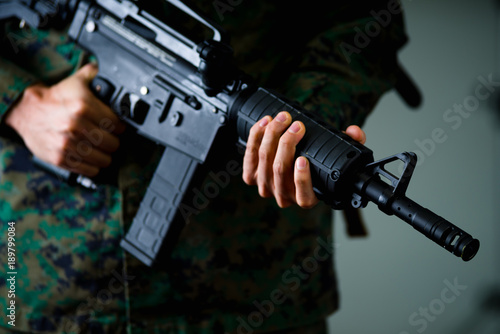 Close up of soldier holding a rifle with both hands and wearing a military uniform, in a gray background