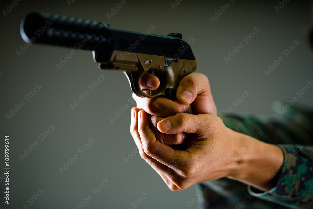 Indoor view of a soldier holding with both hands a gun in gray background Indoor view of a soldier holding with both hands a gun in gray background