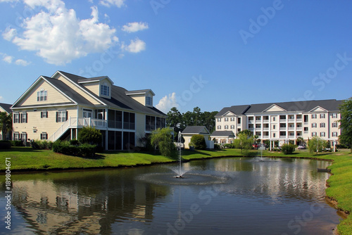 Southern modern architecture and vacation rentals background. Myrtle Beach suburb neighborhood morning view with buildings around the pond with sprinkling fountain. South Carolina, USA.