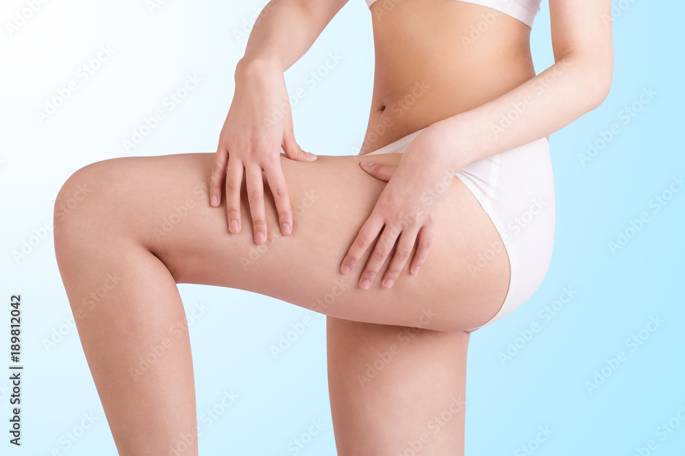 Fit woman touching her thigh. Close up and in white.