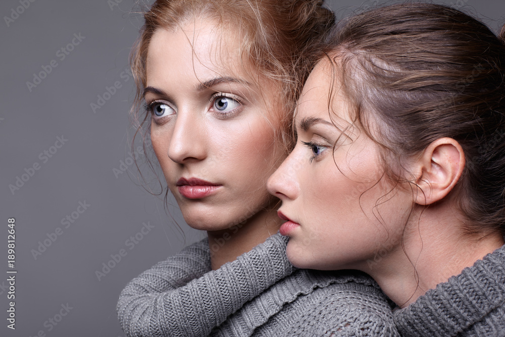 Two young women in gray sweaters on grey background. Beautiful girls stretching hands forward in embrace. Female friendship concept Two young women in gray sweaters on grey background. Beautiful girls stretching hands forward in embrace. Female friendship concept