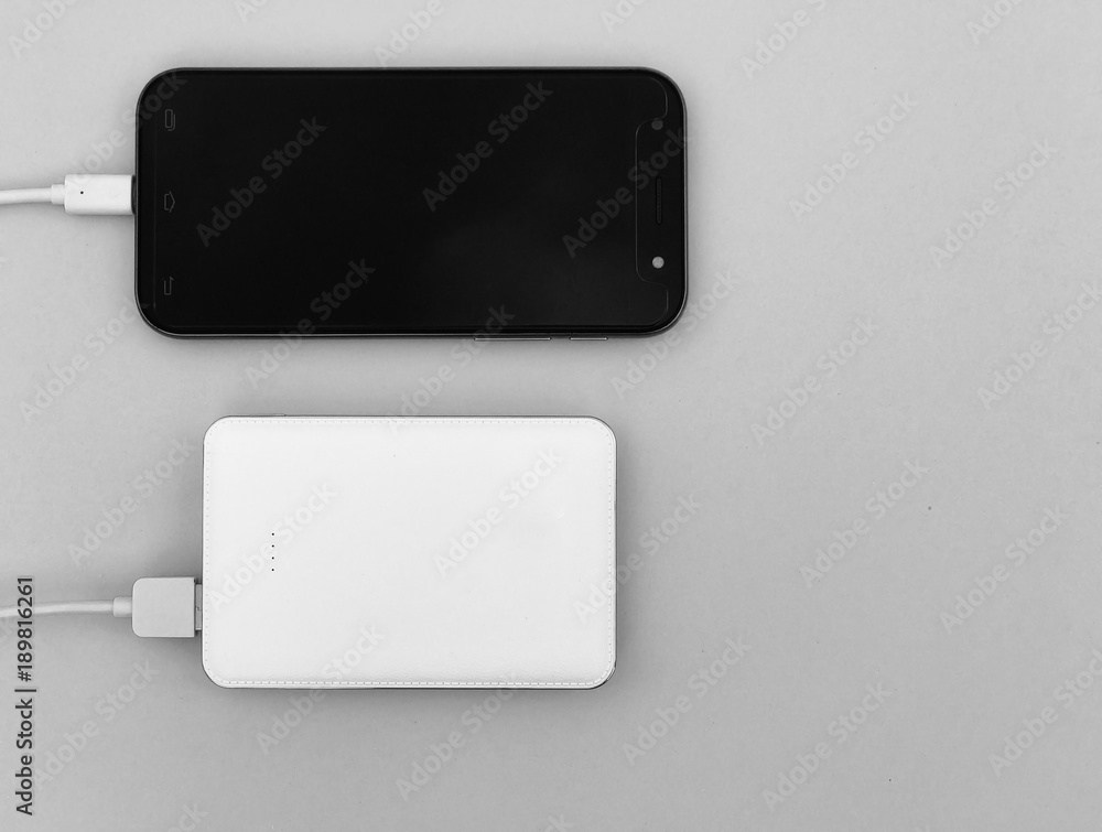 A black smartphone charging with a white powerbank set on gray background. Selective focus with copy space. A black smartphone charging with a white powerbank set on gray background. Selective focus with copy space.