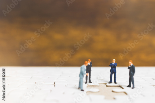 Miniature people: Businessman standing on jigsaw with wooden background