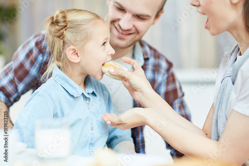 Wallpaper Mural Young careful mother feeding her daughter with fresh and tasty donut at breakfast with father near by Torontodigital.ca