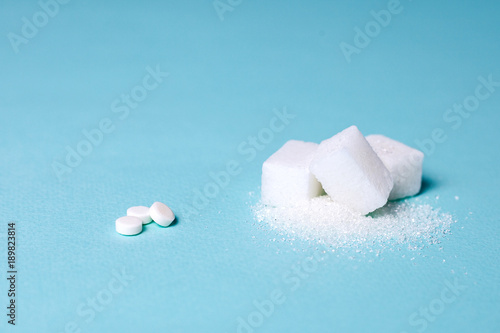 Choice of Sweetener in tablets or regular sugar. Alternative to sugar for people with diabetes. On a green background white sugar in cubes and sugar substitute in tablets