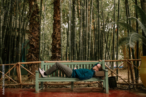 Backpacker man lying on a bench. Man lying on a bench in nature with backpack. Tourist lying on a bench