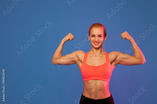 blond female athlete showing biceps on blue background,