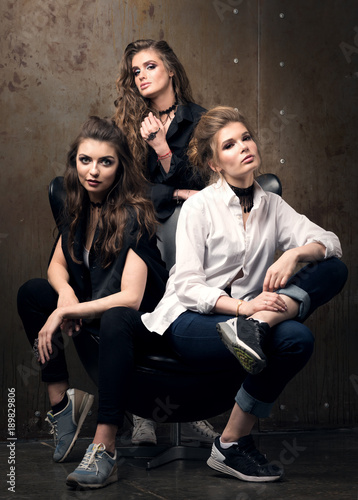 Vertical portrait of three beautiful young women posing on a chair. Modern appearance, professional makeup