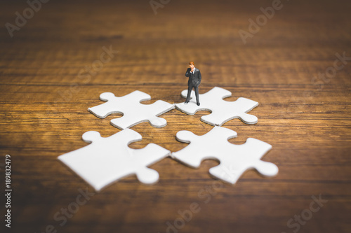 Miniature people: Businessman standing on jigsaw