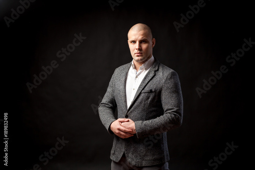 Young bald man in gray suit and white shirt posing on black isolated background