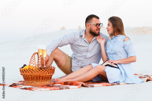 attractive couple sitting together on the white sand beach, looking each other, happy couple enjoying picnic on the beach and have good time on summer vacations, happy couple sitting on a blanket
