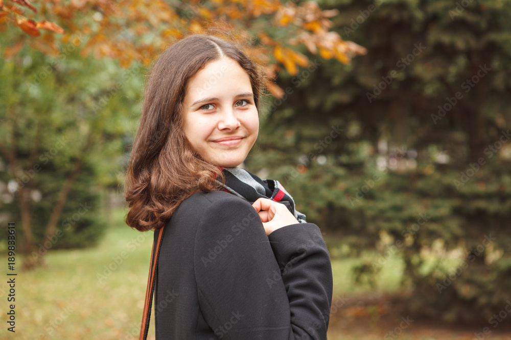 Young beautiful teenage girl turns around and with a smile looks at the camera outdoors. Close-up, autumn. Young beautiful teenage girl turns around and with a smile looks at the camera outdoors. Close-up, autumn.