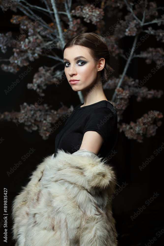 Attractive girl in evening make up and lowered fur coat on dark background Attractive girl in evening make up and lowered fur coat on dark background