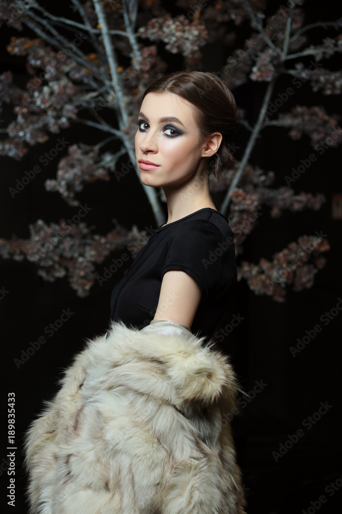 Attractive girl in evening make up and lowered fur coat on dark background Attractive girl in evening make up and lowered fur coat on dark background