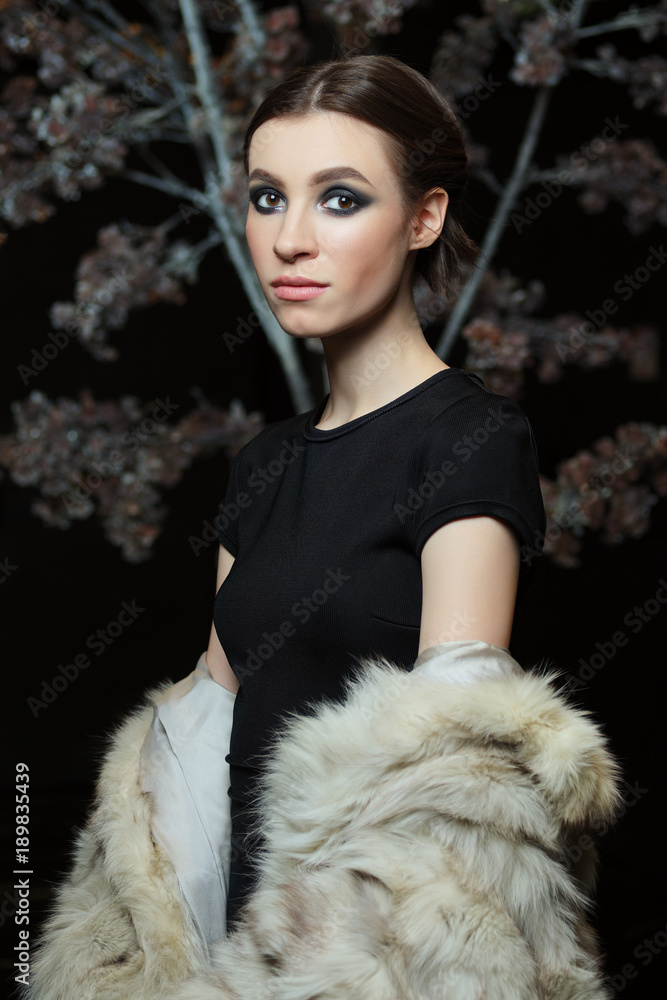 Attractive girl in evening make up and lowered fur coat on dark background Attractive girl in evening make up and lowered fur coat on dark background