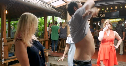 Man dancing with a group of women takes his shirt off in a bar