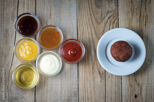 a variety of sauces in glass bowls and a plate with a cutlet on a wooden table