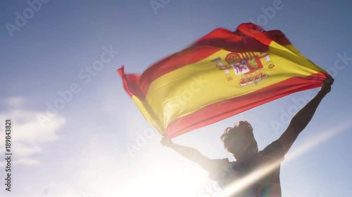 Young man holding spanish national flag to the sky with two hands at the beach at sunset spain photo