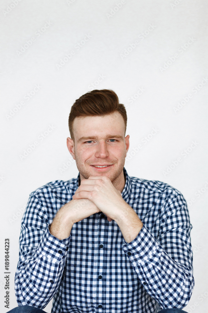 Cheerful handsome redhead young guy in black cardigan checkered shirt photographed against white wall in the studio Cheerful handsome redhead young guy in black cardigan checkered shirt photographed against white wall in the studio