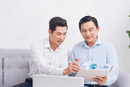 Two confident young businesspeople using a laptop discuss information while sitting on a sofa in a modern office © makistock