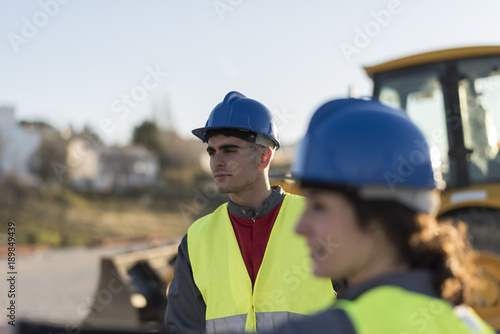 Construction workers talking outdoors near to excavator machine