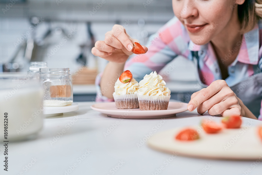 Young female putting strawberry half on top of muffin with whipped cream Young female putting strawberry half on top of muffin with whipped cream
