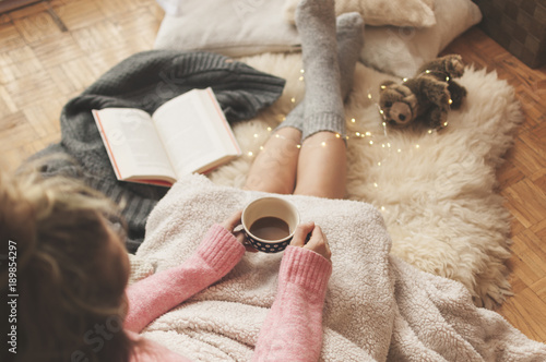 Coziness at home, girl doing hygge with book and warm blanket photo