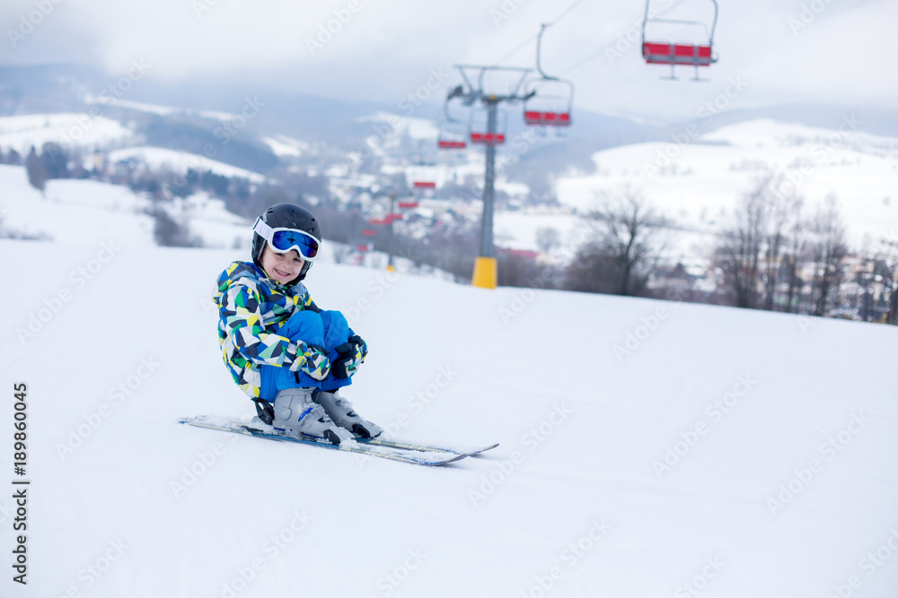 Cute little preschool child in blue jacket, skiing happily on a sunny day