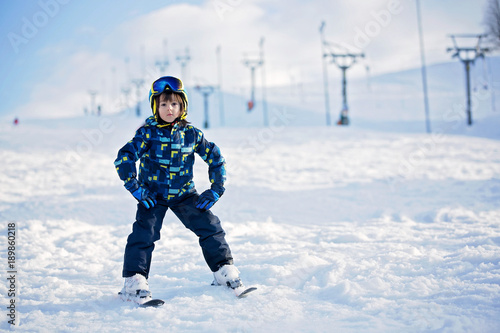 Cute little preschool child in blue jacket, skiing happily on a sunny day © Tomsickova