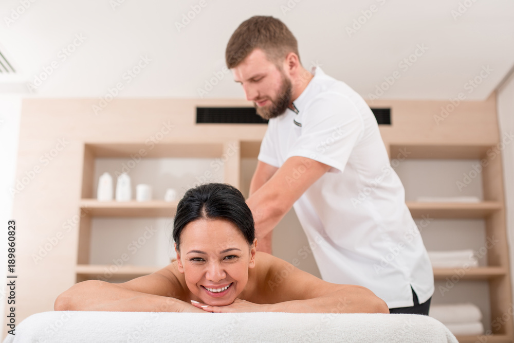 Young masseur giving glad asian woman a massage. Relaxed lady smiling and lying on the couch in beauty salon Young masseur giving glad asian woman a massage. Relaxed lady smiling and lying on the couch in beauty salon