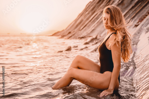 Attractive fit woman in black bikini on ocean with warm sunset colors.