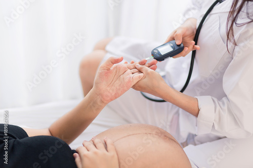 Female Obstetrician doctor measuring blood sugar of the pregnant woman in the hospital. Gestational diabetes mellitus concept.