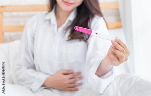 Selective focus Pregnancy test positive result on hand of smiling woman in her bedroom,Blurred background.
