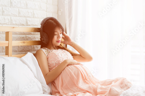 Relaxing Pregnancy woman  in pink dress lisening music from headphone on the bed in bedroom. photo