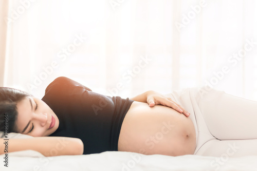  Pregnant woman touching her belly and lying on the bed in bedroom.