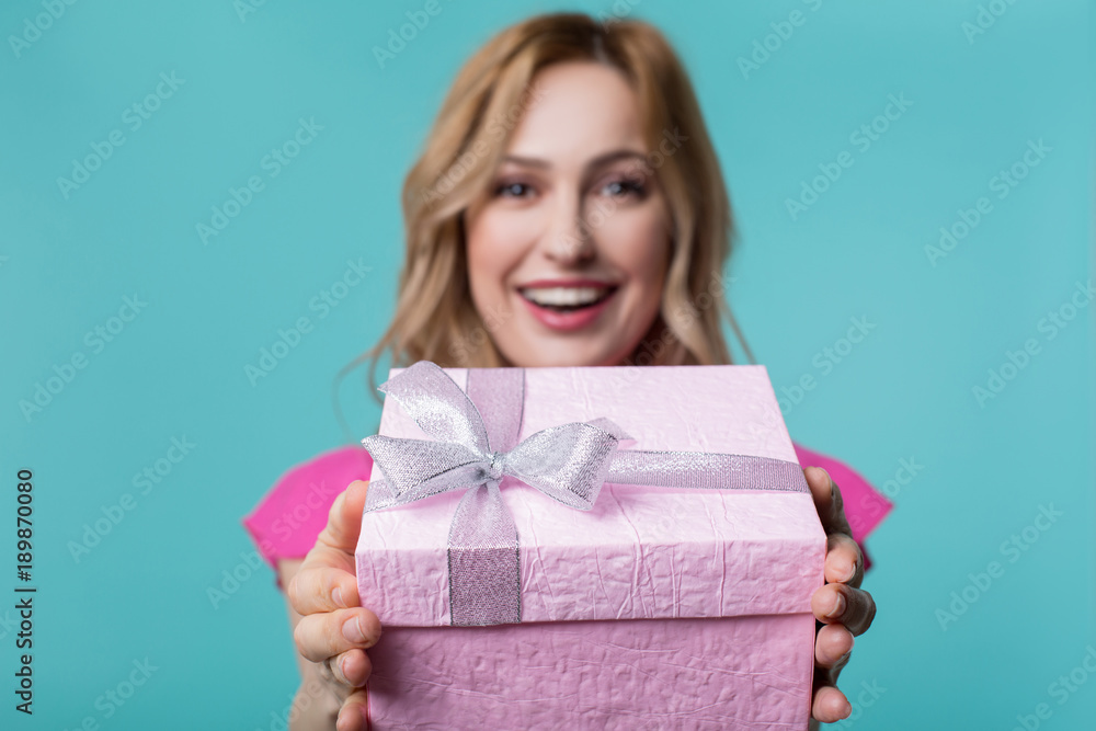 Cheerful young woman is showing pink present box to camera. She is standing and smiling. Focus on present Cheerful young woman is showing pink present box to camera. She is standing and smiling. Focus on present