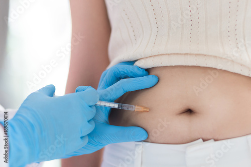 Nurse or doctor in blue glove  holding a syringe with a liquid inject  to a belly of pateint in the hospital  Diabetes treatment.