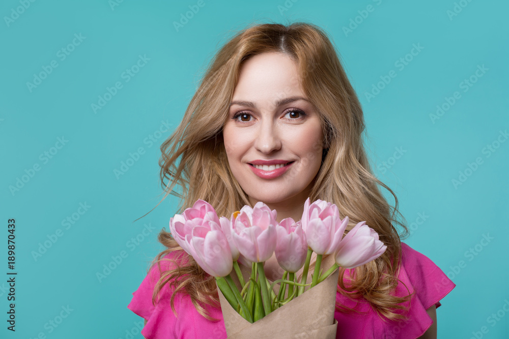 Portrait of happy young woman holding bouquet of tulips. She is looking at camera and smiling. Isolated on blue background Portrait of happy young woman holding bouquet of tulips. She is looking at camera and smiling. Isolated on blue background